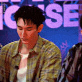 a man in a plaid shirt is sitting in front of a sign that says ' ice ' on it .