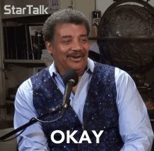 a man sitting in front of a microphone with okay written on his chest