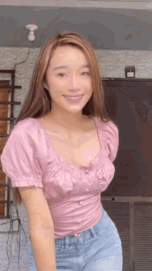 a woman in a pink top and blue jeans smiles