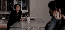 a woman sitting at a table talking to a man who says too late you guys are losers