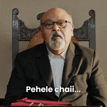 a man with a beard and glasses is sitting in a chair and says pehele chaii