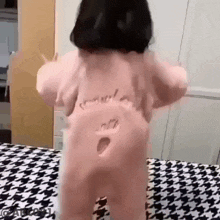 a baby is standing on a bed with a hole in the back of her shirt .