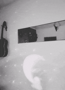 a black and white photo of a guitar hanging on a wall next to a mirror