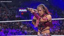 a woman is holding a microphone in a wrestling ring while standing in front of a crowd .