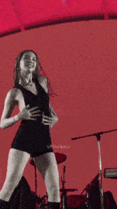 a woman in a black bodysuit is dancing on a stage with a red background and the words @sxrinnz on the bottom