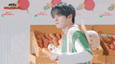 a boy in a green and white striped shirt is holding a carrot in front of a sign that says skz mini world