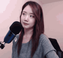 a woman in a grey sweater stands in front of a microphone