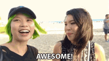 two women are standing on a beach and one has green hair and says awesome