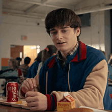 a boy sitting at a table with a can of coca cola