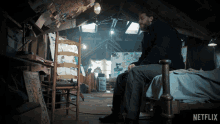 a man sits on a bed in an attic with a netflix logo on the bottom right