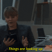 a woman holding a cell phone with the words things are looking up behind her