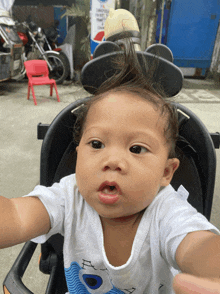 a baby wearing mickey mouse ears is sitting in a stroller and looking at the camera