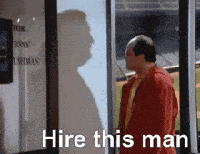a man standing in front of a window with the words " hire this man " written on it