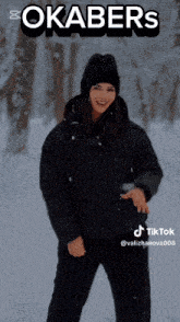 a woman wearing a black jacket and a black hat is standing in the snow with okabers written on the top