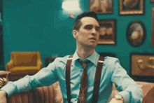 a man wearing suspenders and a blue shirt is sitting on a couch