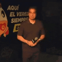 a man is holding a microphone in front of a sign that says aqui el ver siempre