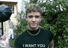 a young man in a black shirt says i want you in front of trees