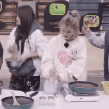 a group of people are standing around a table cooking food in a kitchen .