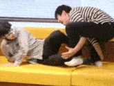 two men are wrestling on a yellow couch and one of them is wearing a blindfold .