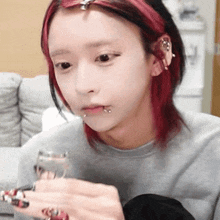 a girl with red hair and piercings on her face holds a glass