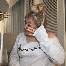 a woman covering her face with her hand and wearing a white shirt that says kmu