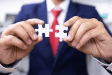 a man in a suit and tie is holding two white puzzle pieces together .