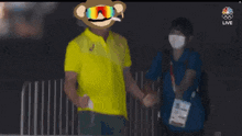 a man in a yellow shirt is standing on a balcony with a monkey head on his head .