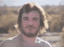 a shirtless man with long hair and a beard is standing in the desert .