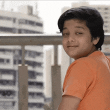 a young boy wearing an orange shirt is smiling and looking at the camera