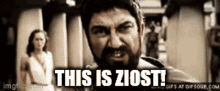 a man with a beard is standing in front of a woman and a sign that says this is ziost .