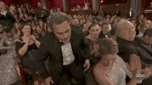 a man in a tuxedo is standing next to a woman in a crowd of people at an awards show .