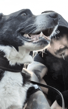 a man with a tattoo on his arm holds a black and white dog in his arms