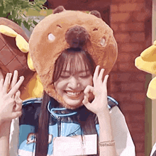 a girl wearing a teddy bear hat is making a peace sign .