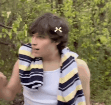 a young man wearing a striped shirt and a towel around his neck is in the woods .