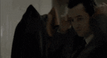 a man in a jacket is looking at a black coat hanging on a rack .