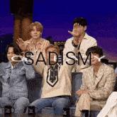 a group of men are sitting on a couch with their hands in the air and the word sadism written on the screen .