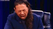 a man in a suit is crying while sitting in a chair with a w live logo in the background .