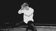 a man in a white shirt and black pants is kneeling down on a stage .