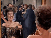 a woman is smiling in front of a mirror while holding a glass