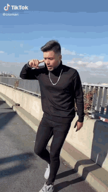 a man wearing a black turtleneck and black pants is standing on a sidewalk with a tiktok watermark on the bottom