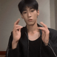 a young man wearing a black jacket and a black tank top making a gesture with his hands
