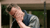 a man in a vest is covering his face with his hands .