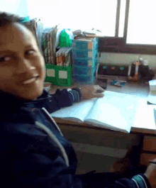 a woman sits at a desk with a book open and smiling