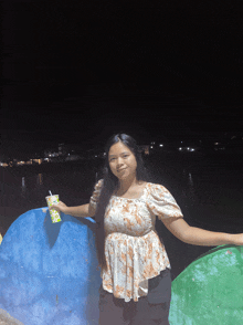 a woman in a floral top is holding a green cup with a straw