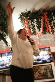 a woman singing into a microphone in a room with flowers on the ceiling