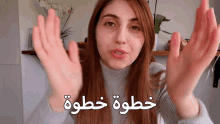 a woman in a grey sweater is making a gesture with her hands in front of her face