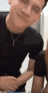 a man and a woman are sitting at a table . the man is wearing a black shirt and a necklace .