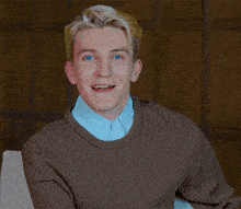 a man with blonde hair is wearing a brown sweater and a blue shirt