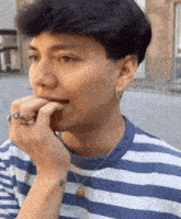 a young man wearing a blue and white striped shirt is biting his finger