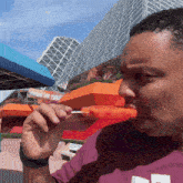a man in a purple shirt is eating an orange popsicle on a stick